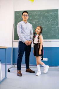 Man and young girl posing in front of a chalkboard filled with math equations, symbolizing education.