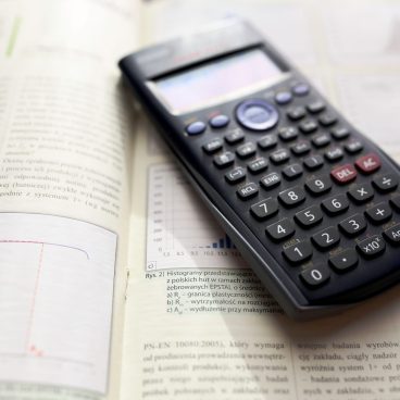 A graphing calculator rests on an open mathematics book with graphs and equations.