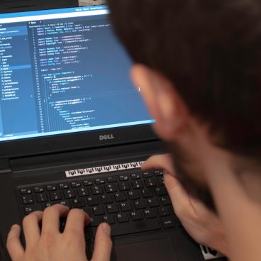 Close-up view of a programmer typing code on a laptop in a workspace.